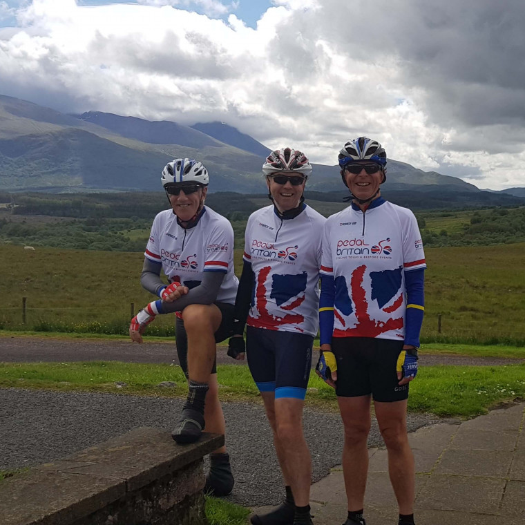 Three lejog cyclists having their picture taken in front of a beautiful landscape.