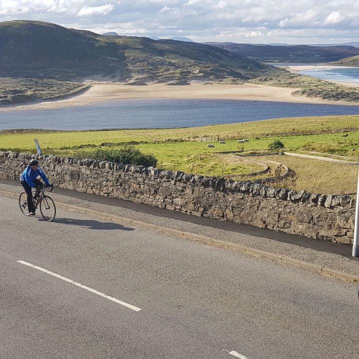 cyclists riding up hill with sea in background